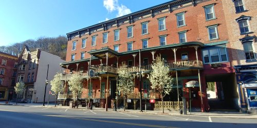 Historic brick building with balconies, surrounded by blooming trees, on a quiet street under a clear blue sky.