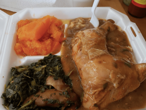 A takeout container with chicken in gravy, collard greens, and sweet potato mash.