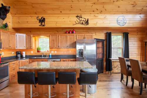 A rustic kitchen with wooden walls, granite island, black bar stools, and decorative animal art on the ceiling.