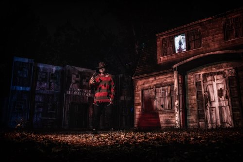 A figure in a striped sweater and hat stands in front of a spooky, dimly lit house at night.