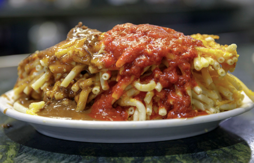 A plate of macaroni topped with chili and red sauce, showcasing a hearty, comforting meal.