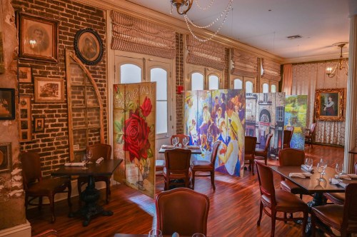 A cozy restaurant interior with wooden tables, chairs, and colorful art panels separating dining areas.