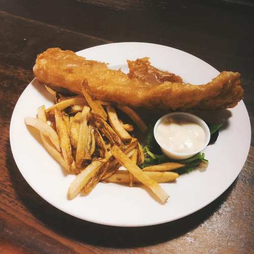 A plate of golden fried fish with a side of crispy fries and a small cup of dipping sauce.
