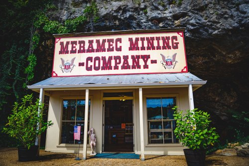 Front view of the Meramec Mining Company building, featuring a sign and greenery, set against a rocky backdrop.