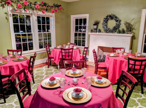 A cozy dining room with pink tablecloths, elegant place settings, and floral decor on the walls.