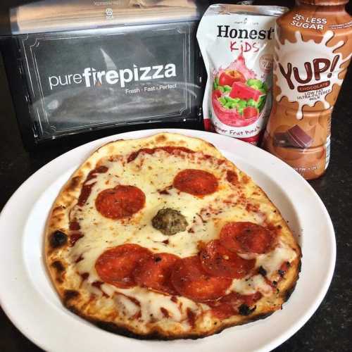 A pizza with pepperoni and cheese, accompanied by a drink and snacks, on a table with a pizza box in the background.