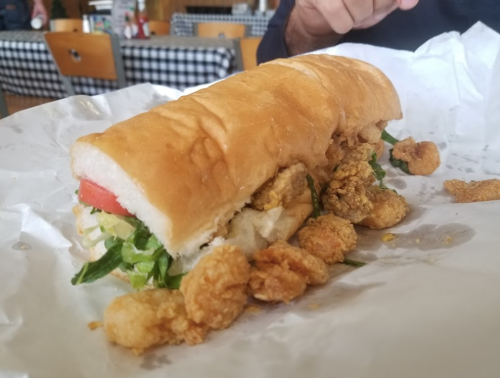 A sandwich filled with lettuce, tomato, and fried shrimp, resting on crumpled white paper.