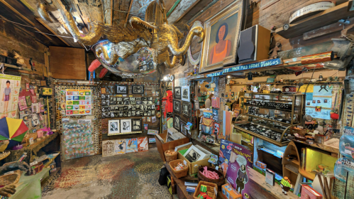 A vibrant, eclectic shop filled with art, photographs, and unique decor, featuring colorful walls and various displays.