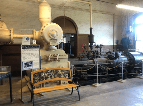 Historic pumping station interior featuring large machinery and a decorative bench. Informational sign visible.