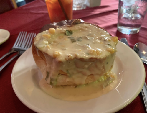 A bowl of creamy seafood chowder served in a bread bowl, placed on a white plate with utensils nearby.