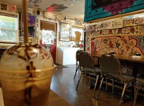 A cozy café interior with colorful wall art, empty chairs, and a chocolate drink in the foreground.