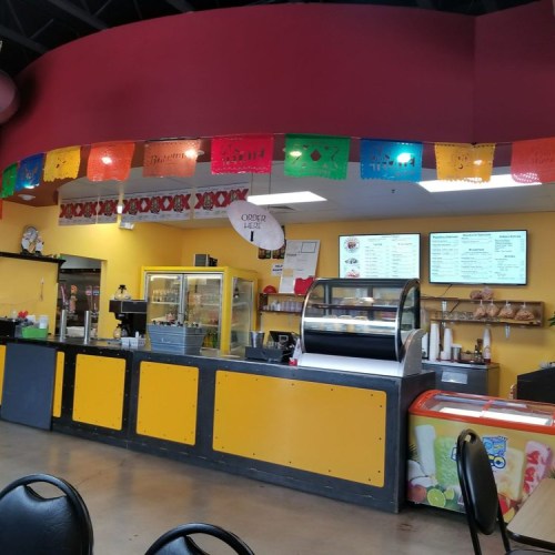 A colorful restaurant interior with a service counter, menu boards, and festive decorations hanging from the ceiling.