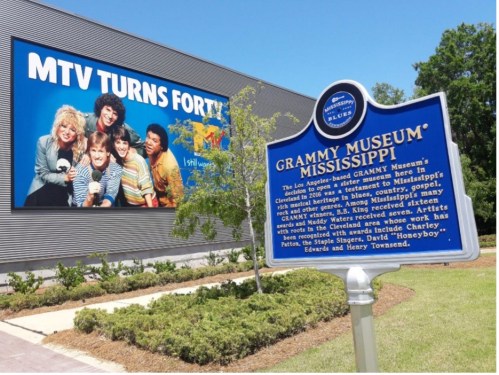 Sign for the Grammy Museum Mississippi with a colorful mural of musicians in the background. Bright, sunny day.