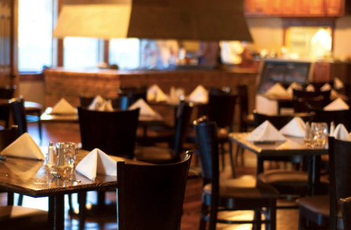 Cozy restaurant interior with wooden tables, neatly folded napkins, and an open kitchen in the background.