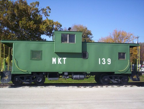 A green caboose marked "MKT 139" parked on a gravel track with trees in the background.
