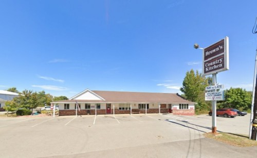 Exterior view of Brown's Country Kitchen, a single-story building with a sign, surrounded by trees and a clear blue sky.
