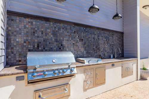 Outdoor kitchen featuring a stainless steel grill, countertop, and decorative tiled backsplash.