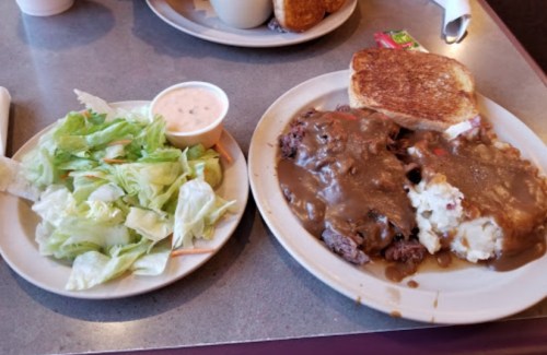 A plate with beef covered in gravy, mashed potatoes, and toast, alongside a small salad with dressing on the side.