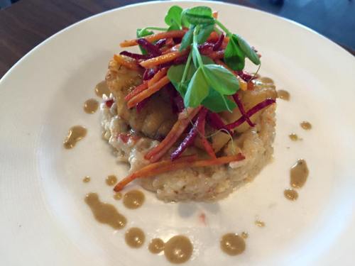 A plate of risotto topped with fried fish, colorful vegetable strips, and drizzled with sauce.