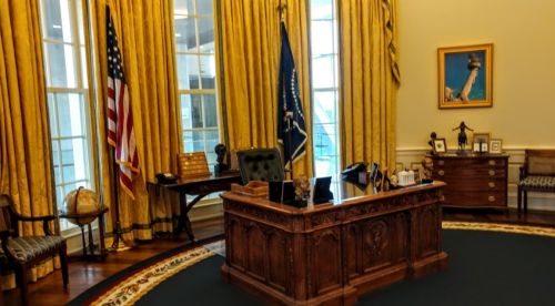 A well-furnished office with a large wooden desk, yellow curtains, and an American flag, featuring a globe and various decor.