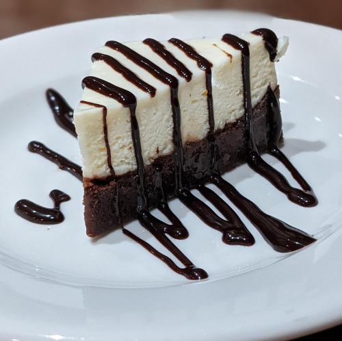 A slice of cheesecake with a chocolate drizzle on a white plate.