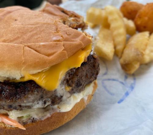 A close-up of a cheeseburger with melted cheese, lettuce, and mayonnaise, accompanied by crinkle-cut fries and tater tots.
