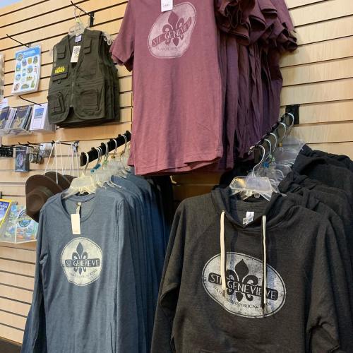 A display of t-shirts and hoodies in various colors hanging on a rack against a wooden wall.