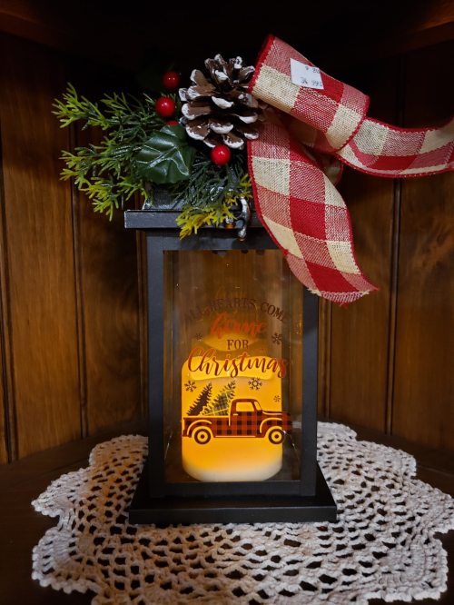 A decorative lantern with a plaid ribbon, pinecone, and greenery, featuring a warm "Love for Christmas" design.