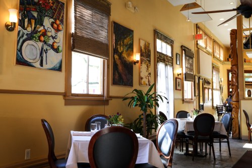 Cozy restaurant interior with tables set for dining, colorful artwork on the walls, and natural light from windows.