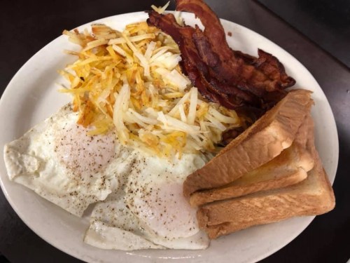 A plate of breakfast featuring two fried eggs, crispy bacon, hash browns, and toasted bread.