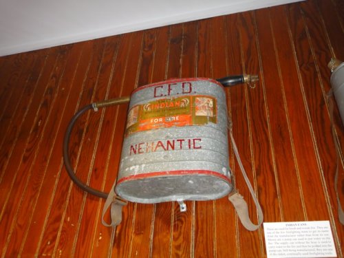 A vintage fire extinguisher mounted on a wooden wall, labeled "C.F.D. Nehantic" with a red and yellow design.