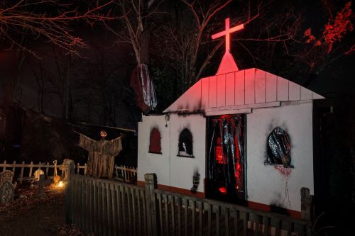A spooky, dimly lit haunted house with a cross, eerie decorations, and a ghostly figure in a graveyard setting.