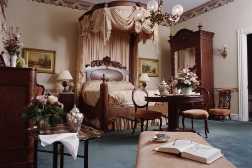 Elegant bedroom featuring a four-poster bed, antique furniture, floral decor, and a cozy seating area.