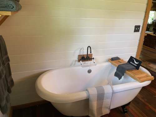 A cozy bathroom featuring a freestanding bathtub with a wooden tray, towels, and a rustic wooden wall.