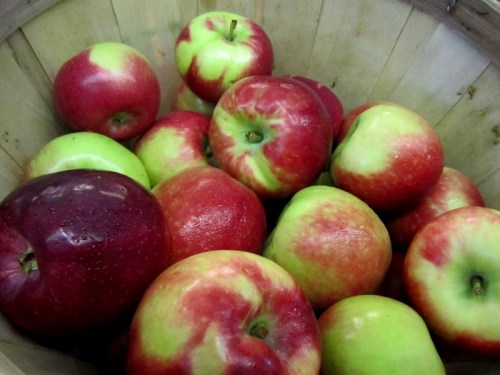 A wooden basket filled with a variety of red and green apples.