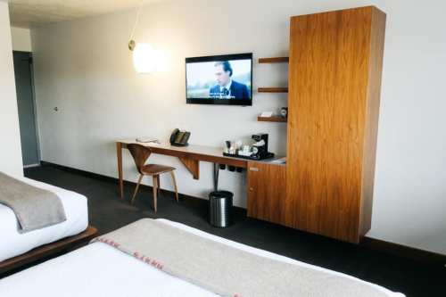 A modern hotel room featuring two beds, a wooden desk, a TV on the wall, and a coffee station.