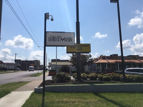 Sign for Market on Main with a promotion for sausage biscuits and coffee, alongside a McDonald's in the background.