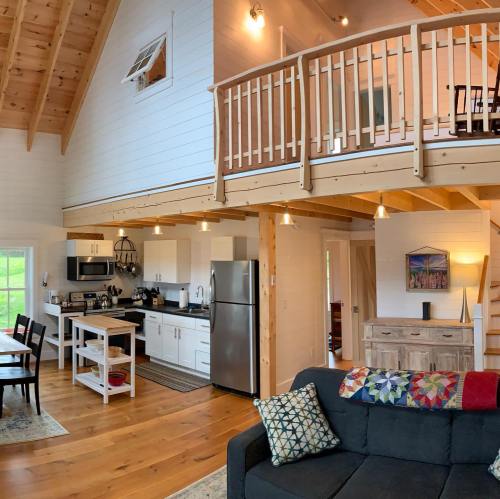 Cozy interior of a cabin with wooden beams, a kitchen, dining area, and a living space featuring a sofa and decor.