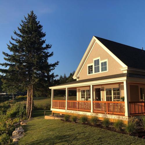 A charming house with a porch, surrounded by greenery and trees, under a clear blue sky during sunset.