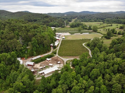 Aerial view of a lush green landscape with farms, fields, and winding roads surrounded by trees and hills.