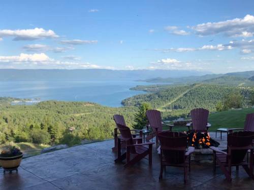 Scenic view of a lake and mountains from a patio with Adirondack chairs and a fire pit.