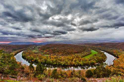 A winding river curves through a colorful autumn landscape under a dramatic, cloudy sky.