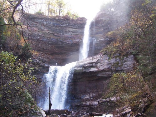 A stunning waterfall cascades down rocky cliffs, surrounded by lush greenery and trees in a serene natural setting.