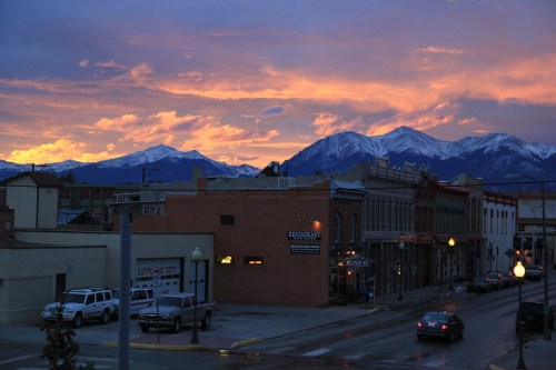 Sunset over a mountain town, with colorful skies and snow-capped peaks in the background.