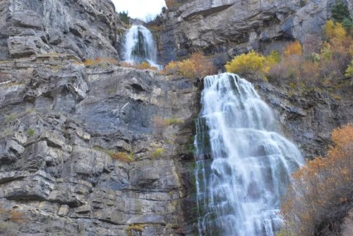 A scenic view of cascading waterfalls flowing down rocky cliffs, surrounded by autumn foliage.
