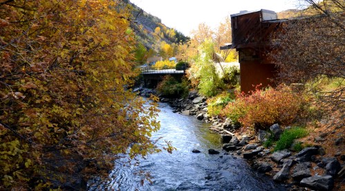 A serene river flows through a landscape of autumn foliage and rocky banks, with a modern building in the background.