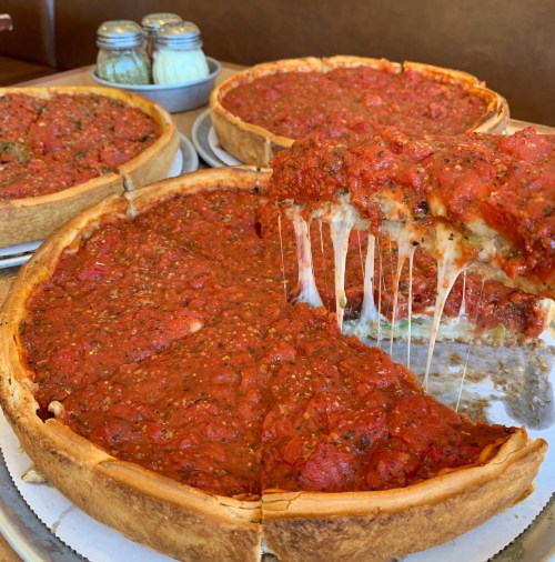 A close-up of a deep-dish pizza with a slice pulled out, showcasing melted cheese and a rich tomato topping.