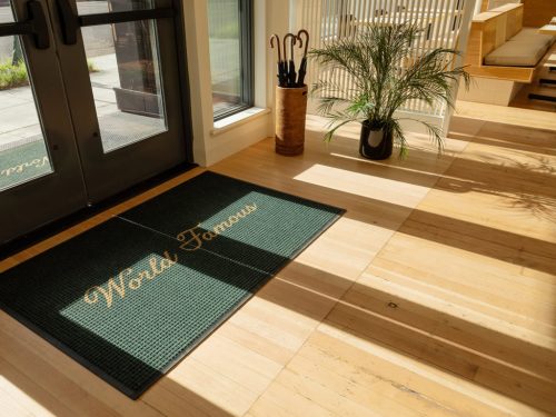 A welcome mat reading "World's Famous" at the entrance, with sunlight streaming in and plants nearby.