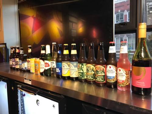 A variety of beer bottles and a wine bottle lined up on a counter, with a colorful background.