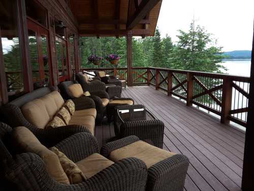 Cozy outdoor seating area on a wooden deck overlooking a serene lake and lush trees.